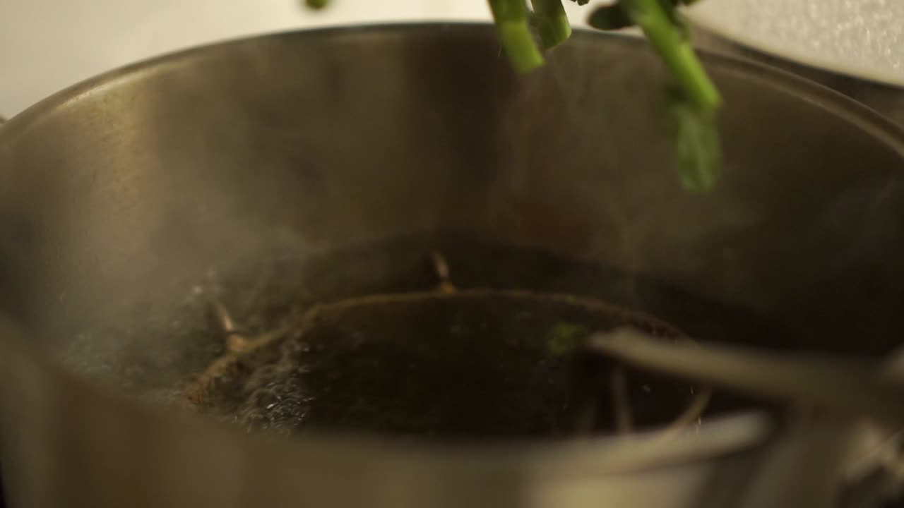 Nærbillede - Kok lægger en rå broccoli i en gryde med varmt vand i et restaurantkøkken