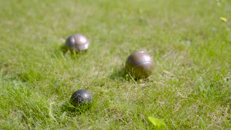 Close-up-view-of-three-metal-petanque-balls-on-the-grass,-then-the-player-throw-another-ball-nearby