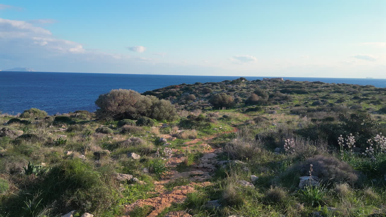 Experience the breathtaking beauty of Athens with a low-flying drone capturing serene landscapes of shrubs and stones, as it heads towards the sparkling sea under a clear blue sky in February.