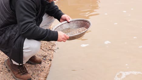 person panning for gold in muddy water