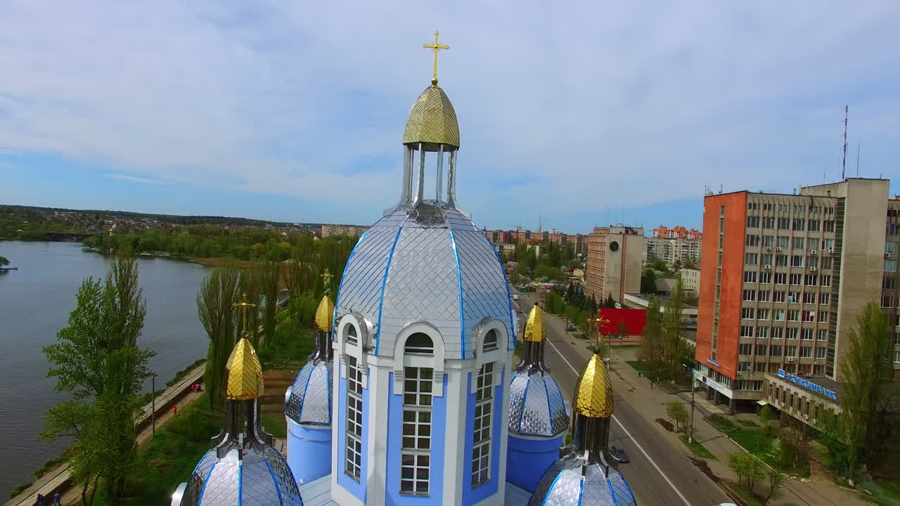 Drone footage distancing from the blue building of Orthodox church. Downtown of Ukrainian city with river in the centre. Top view.