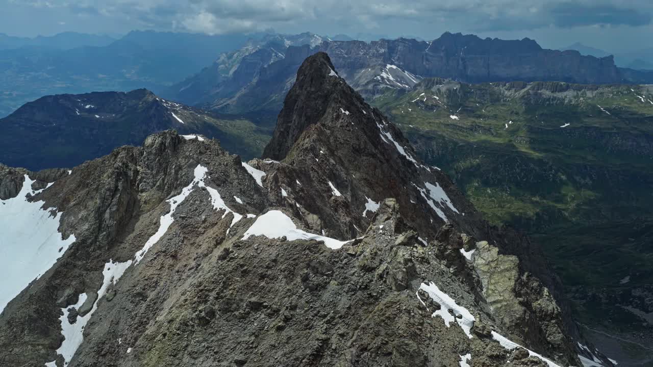 Una ripresa aerea in allontanamento che rivela il maestoso paesaggio delle Alpi francesi a Chamonix, con una cima montuosa innevata e frastagliata e una profonda valle glaciale in una giornata limpida.