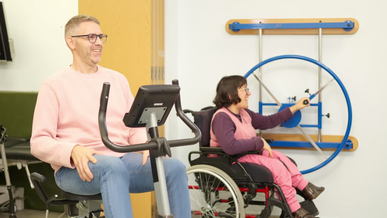 Man on Exercise Bike and Woman in Wheelchair in Rehabilitation Center