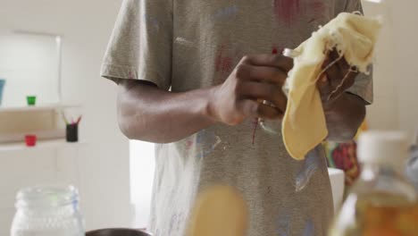 Mid-section-of-african-american-male-artist-cleaning-his-hands-at-art-studio