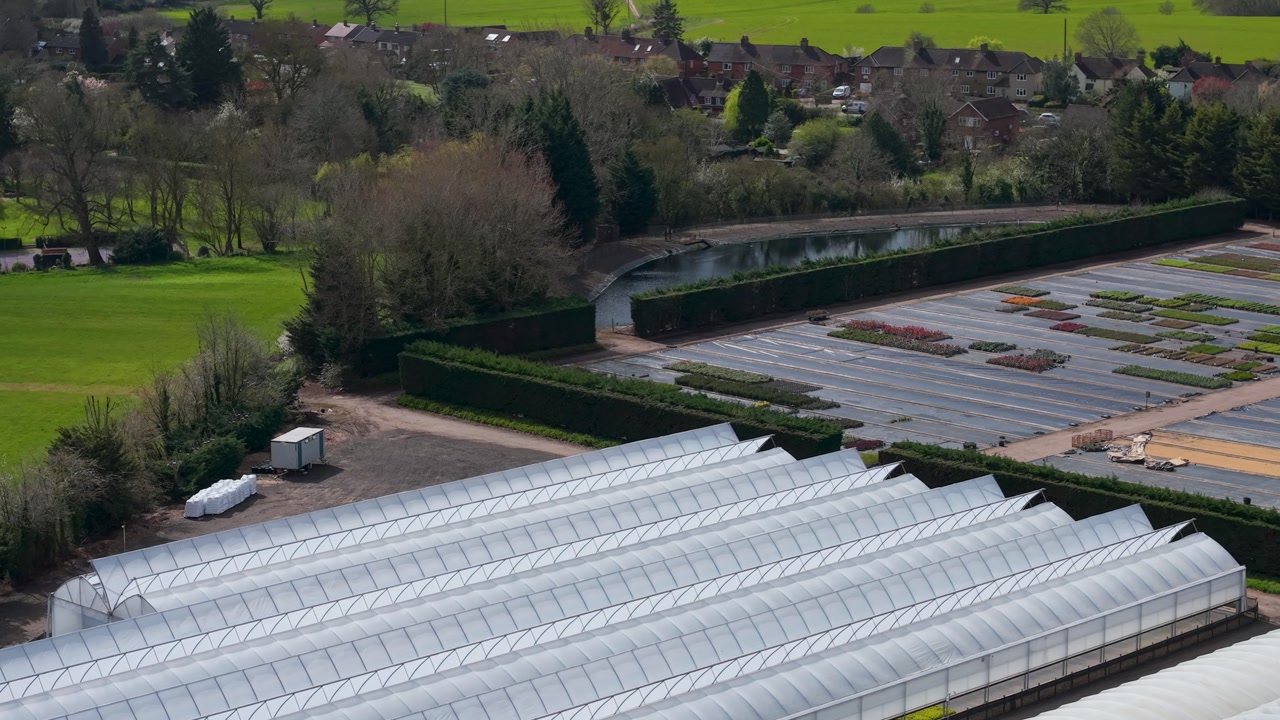Drone flight over greenhouses and open planting beds with crops growing through black plastic sheeting in Birch Green, Hertfordshire, England, showcasing modern horticulture.