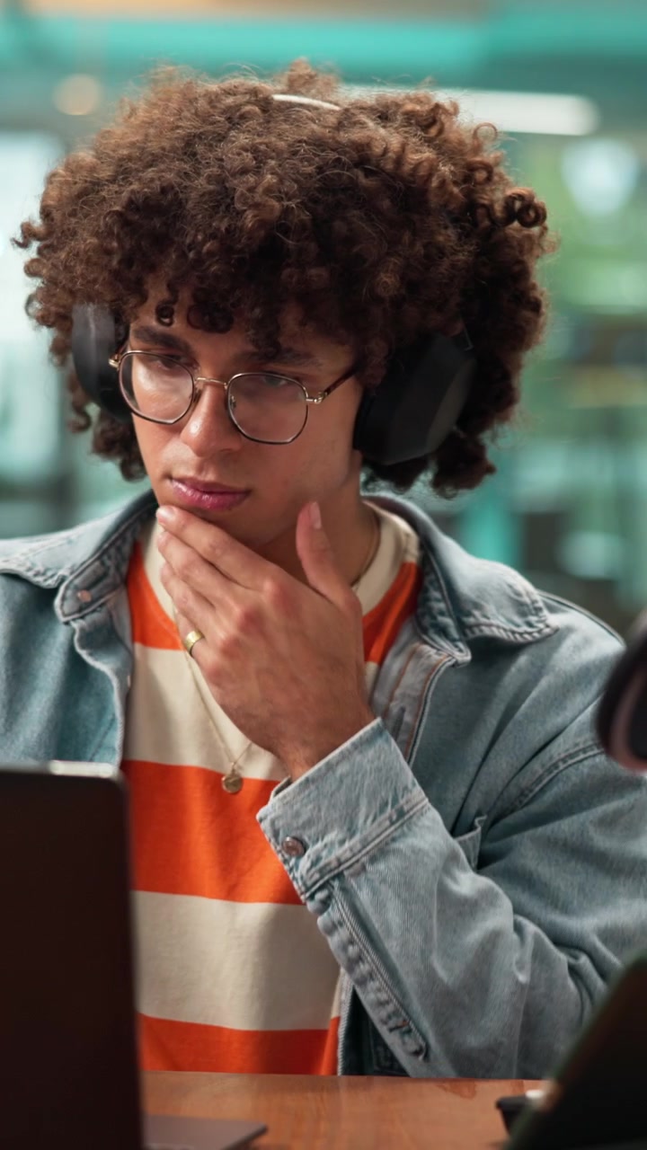 Young Man with Curly Hair Working on Laptop in Office