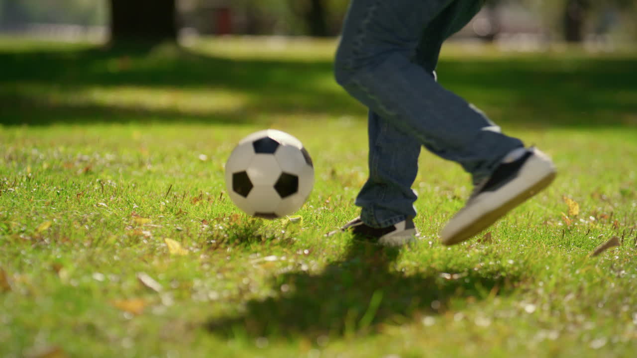 las piernas de primer plano pateando la pelota de fútbol en el campo verde. verano activo fin de semana en el parque