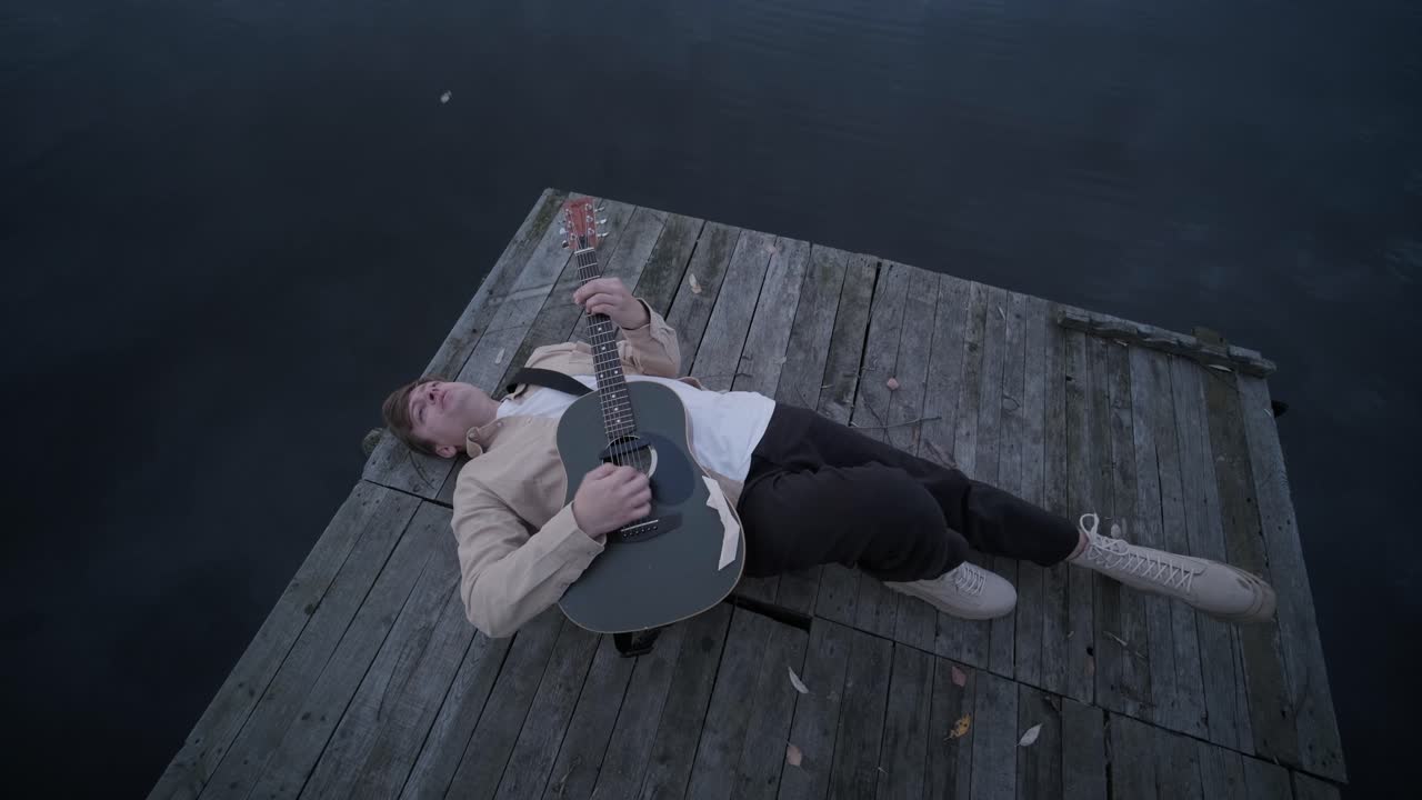 Man Playing Guitar On Lake Pier