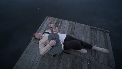 man playing guitar on lake pier