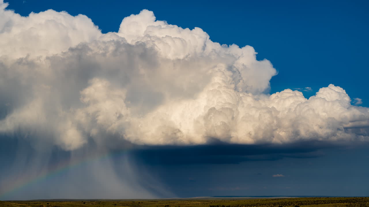 Puffy white storm clouds and rainbow drift across colorful sky