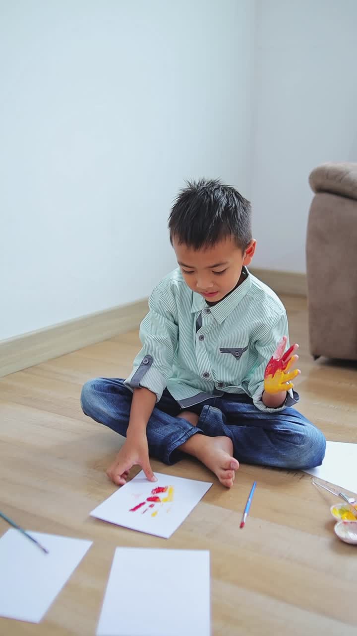 Young asian boy creatively painting on paper while sitting on the floor