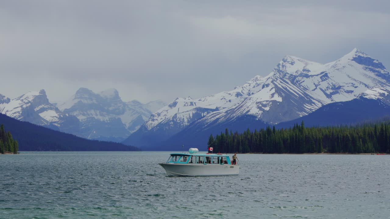 Barca turistica che naviga sul lago Maligne con montagne innevate nel parco nazionale di Jasper, Canada.