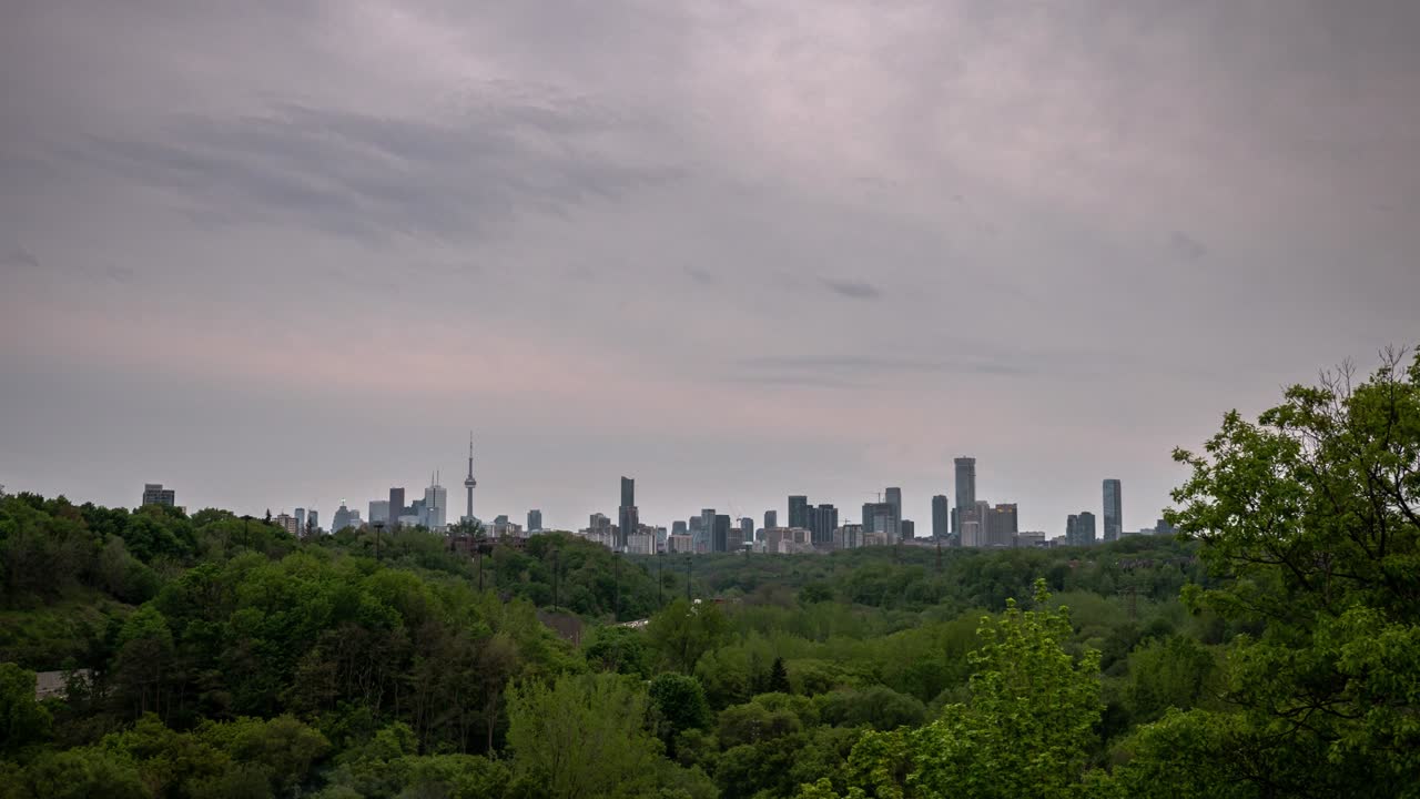 캐나다 토론토의 시내 스카이 라인의 타임 스 (timelapse) 는 해가 지는 동안 구름이 많은 분홍색과 파란색 하늘과 함께 나무의 숲으로 둘러싸인 인근 고속도로에서 교통이 지나갈 때입니다.