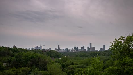 timelapse del horizonte de la ciudad en toronto, canadá, durante la puesta de sol con un cielo rosado y azul nublado mientras el tráfico pasa por una autopista cercana rodeada de un bosque de árboles.