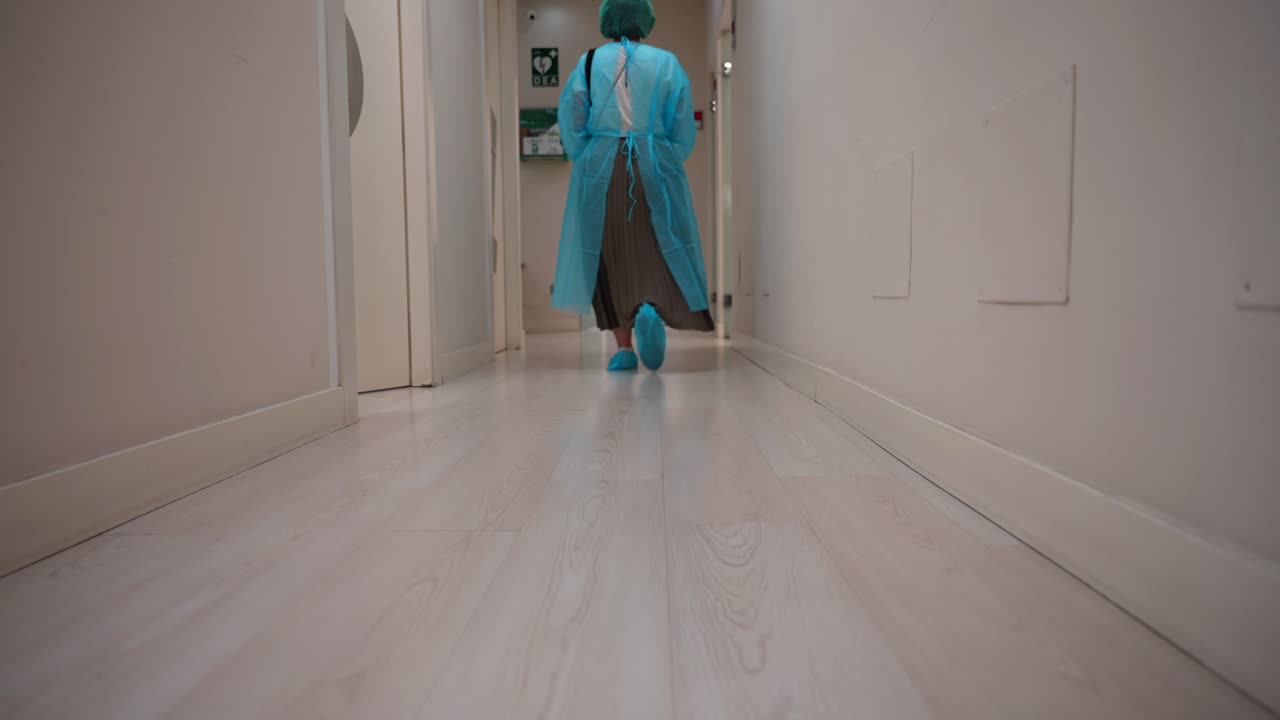 Person in Protective Clothing Walking Down a Hospital Hallway
