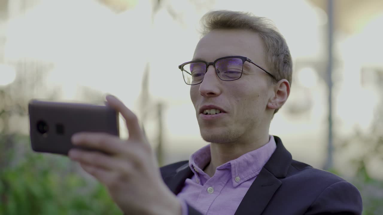 joven sonriente con gafas haciendo una videollamada por teléfono