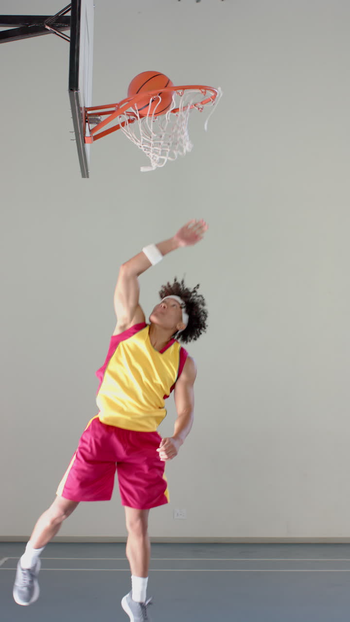 Vertical video: Jumping to dunk basketball, male athlete in sportswear reaching hoop