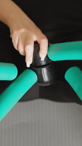 mujer hace ejercicios con un dispositivo de tonificación del muslo en primer plano. entusiasta del fitness utiliza un entrenador de músculos de las piernas sentado en el suelo en el área de fitness personal. mejora del cuerpo