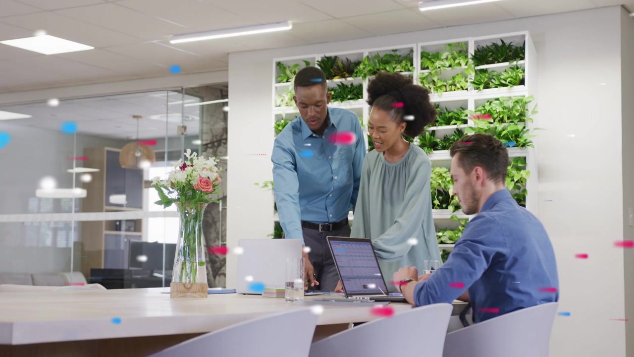 2 coworkers leaning and pointing at laptop in office, initiating task, particles floating on screen