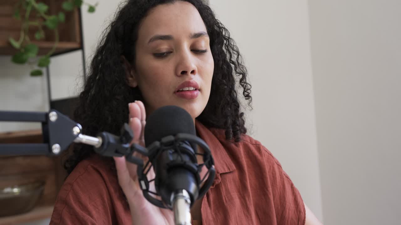 Donna afroamericana che digita, si ferma, allunga la mano verso il microfono, con una camicia color ruggine alla scrivania, mentre testa l'audio sul laptop.