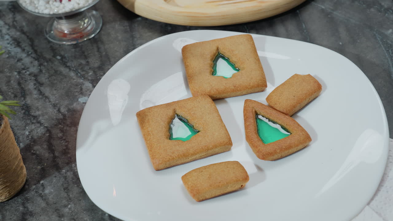 색 접시 위에 쿠키와 함께 장식 된 꽃의 클로즈업, 안쪽에서 볼 수 있는 녹색 채우기, 배경에 더 많은 쿠키가있는 나무 트레이, 축제적인 호소력으로 집에서 만든 장식 된 쿠키를 보여줍니다.