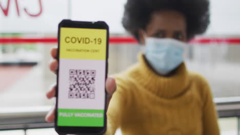 mujer de negocios afroamericana con máscara preparando la certificación de covid-19 en su teléfono inteligente