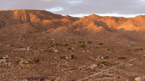 aerial view of little houses and dirt road in joshua tree at sunrise on a pretty morning with jagged hills in the background