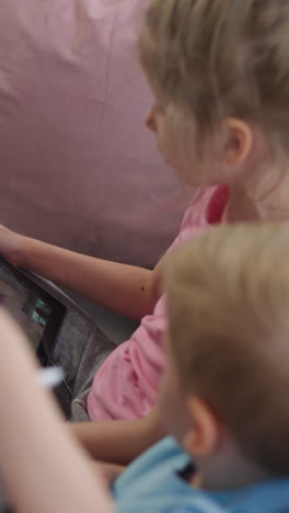 preschooler girl and toddler boy talk with grandma on video call via modern tablet. little boy shows granny airplane toy sitting on sofa closeup