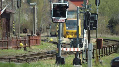 a railway crossing closed with signals flaring as the train is waiting at the station