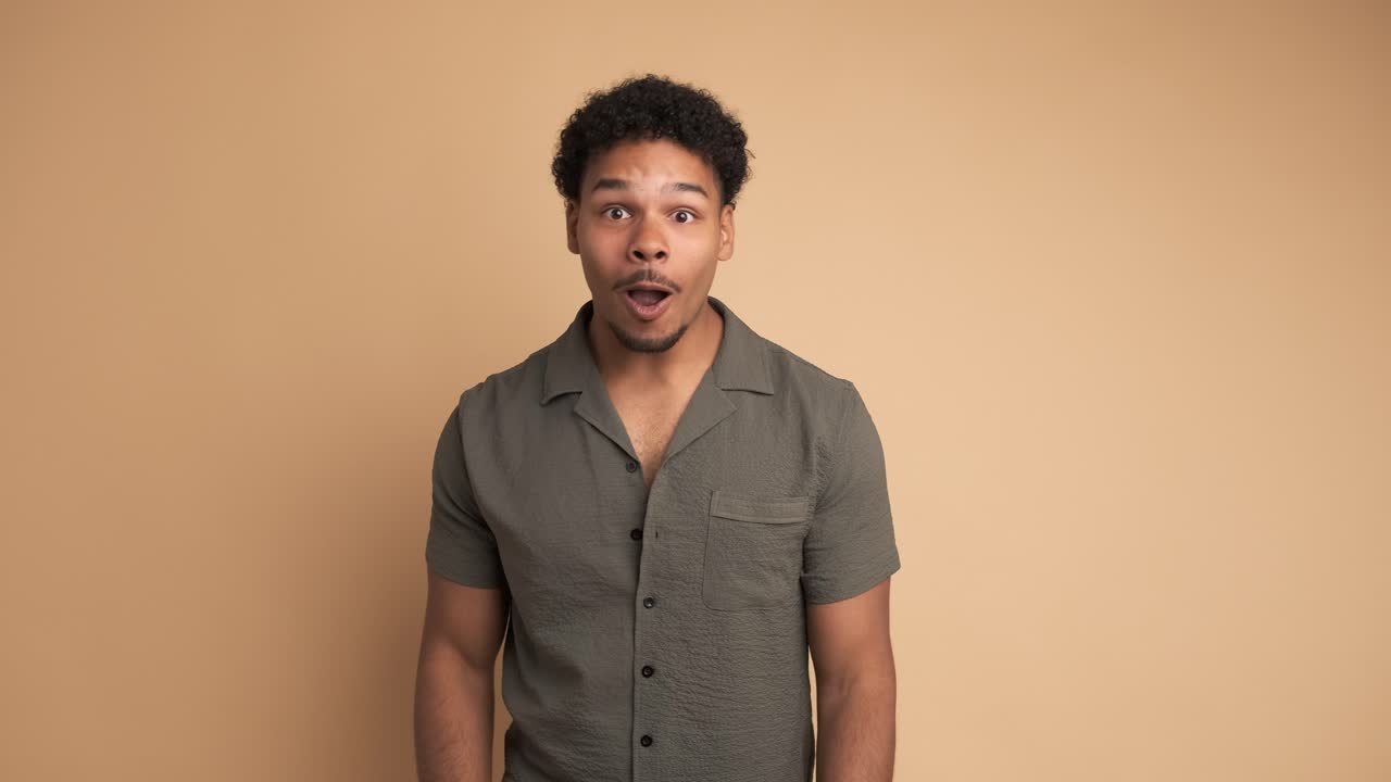 Surprise young man smiling at camera in beige studio
