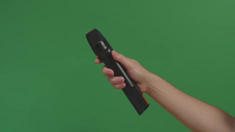 male hand holding microphone against background green screen chroma key. close up mic, interview, live press conference, karaoke, singer performance