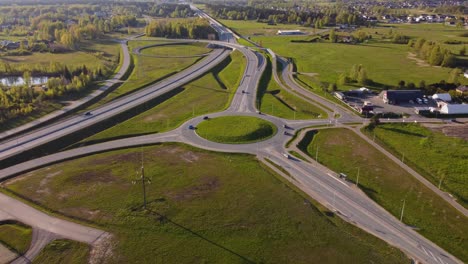 aerial view of cars driving on roundabout and highway in katlakalns residential area, latvia during spring, surrounded by green fields and trees