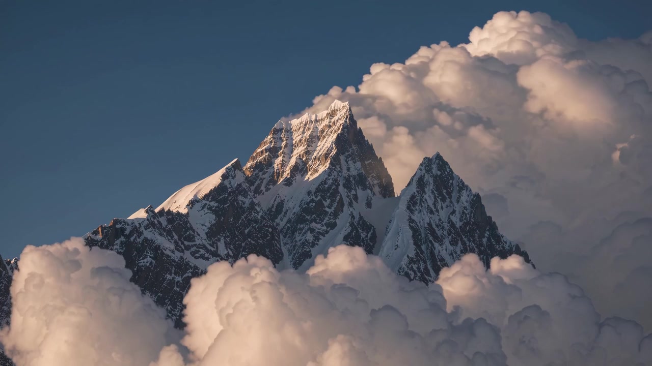 Vetta montuosa innevata che si innalza sopra nuvole dense al tramonto