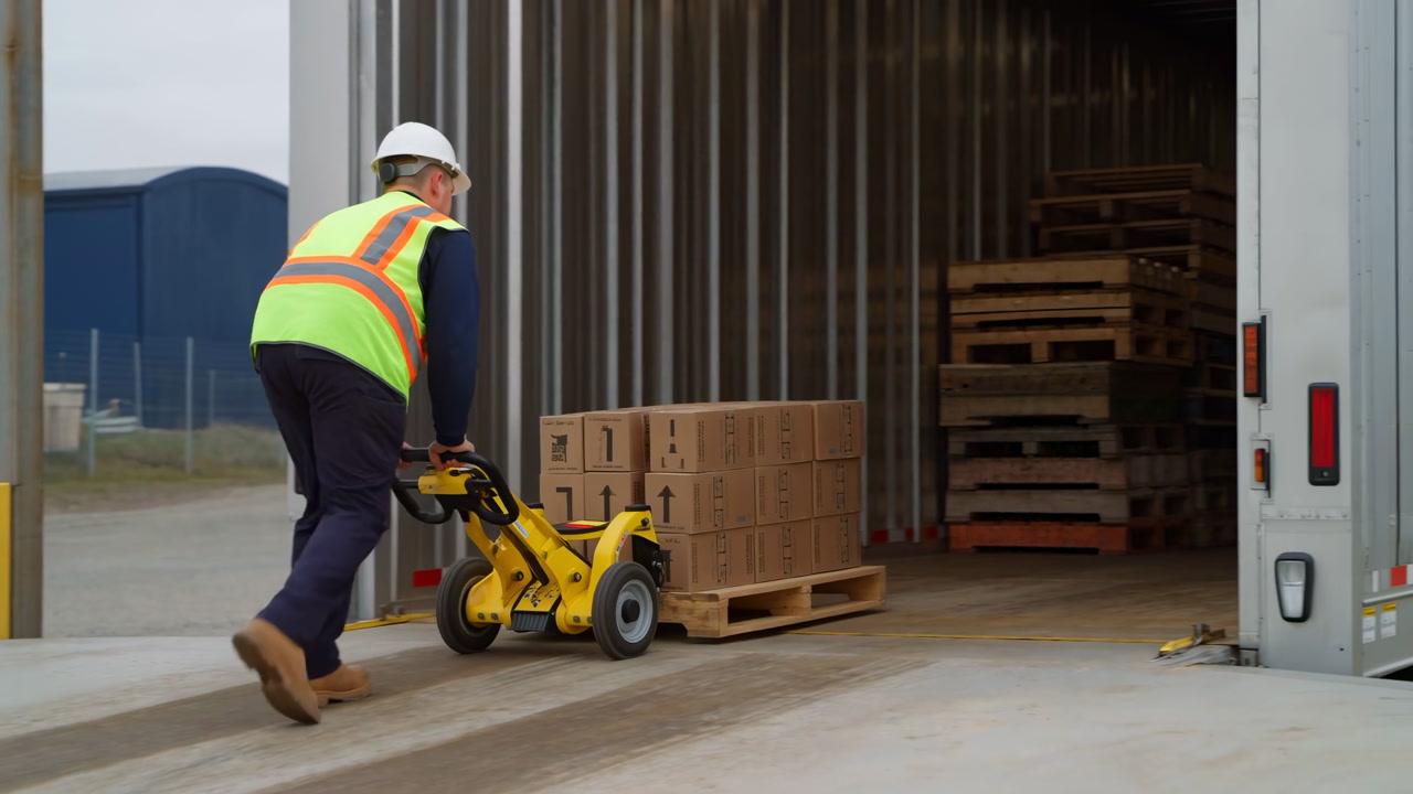 Warehouse Worker Pushing Pallet Into Trailer Using Dolly, Wearing Helmet And Highvisibility Vest, Stacking