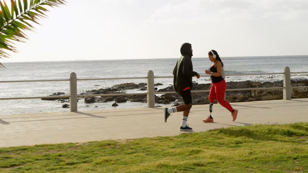 vista lateral de una pareja corriendo en el paseo marítimo en un día soleado 4k