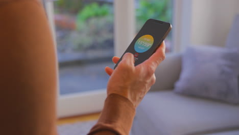 close up of man at home looking at app on smart phone to control heating