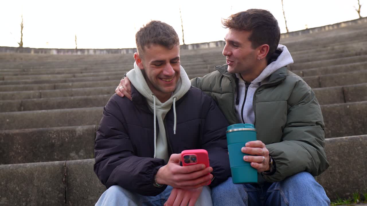 Two young men sitting on stairs using a phone