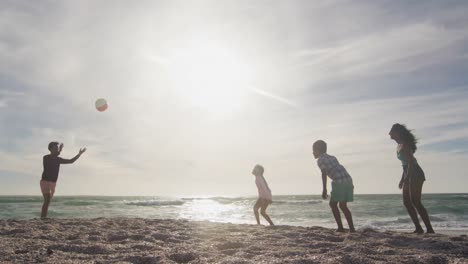 happy hispanic mother, father, son and daughter playing with ball on beach