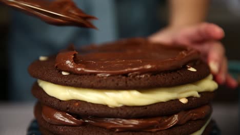 spreading chocolate frosting on a multi-layered cake filled with cream