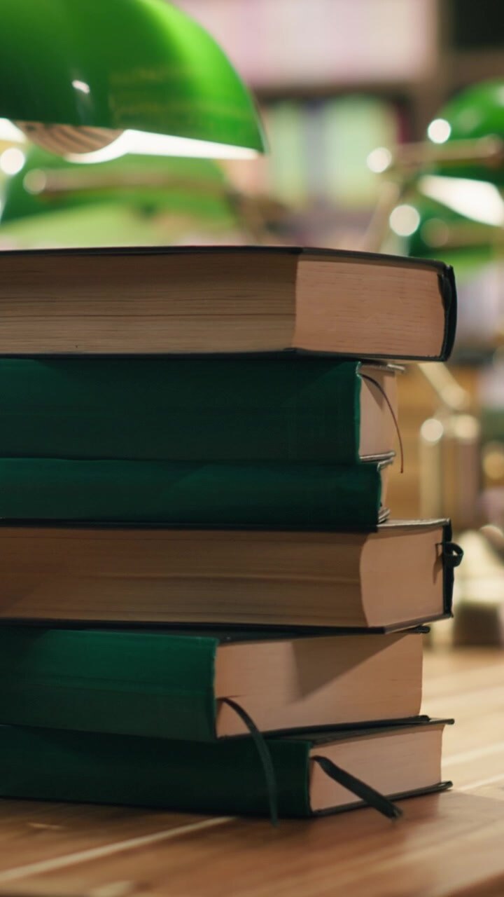 Video verticale: Pila di libri verdi con copertina rigida su una scrivania di biblioteca con scaffali sfocati.