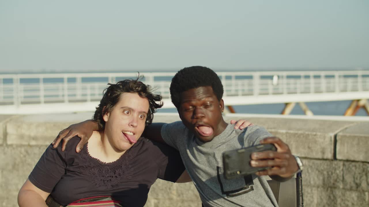 pareja graciosa usando sillas de ruedas haciendo caras y tomando selfies