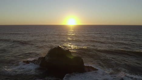 large ocean waves crash and splash water spray up into air as sun dips below horizon