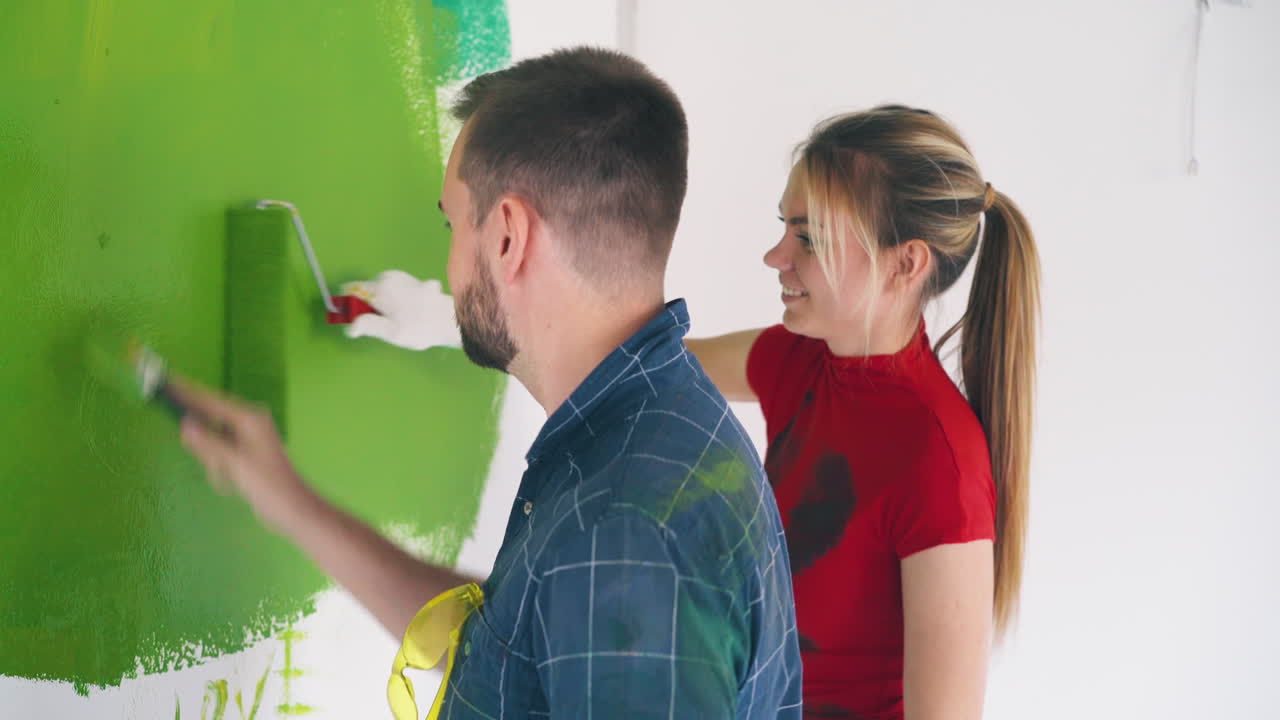 hombre positivo con mujer pintando la pared con color verde en la habitación