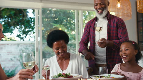 Familia-Multigeneracional-Sentada-Alrededor-De-La-Mesa-Bebiendo-Vino-Antes-De-Comer-En-Casa-Juntos