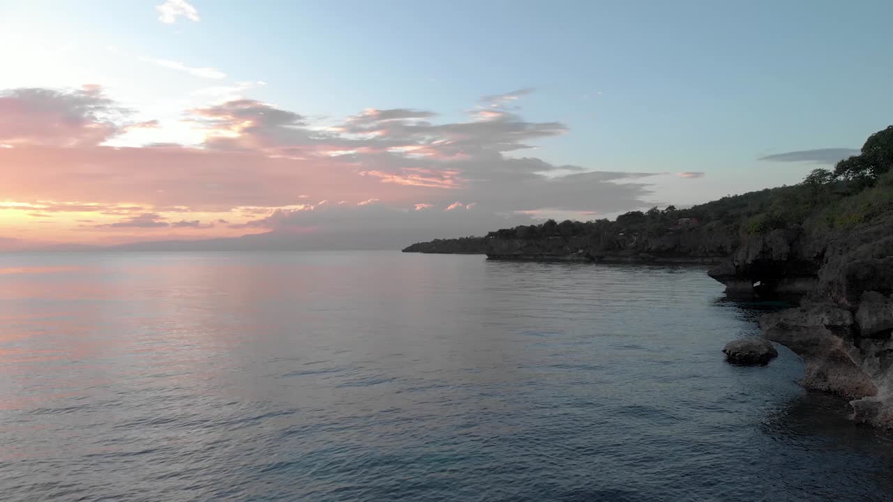 toma cinematográfica aérea de una hermosa y vibrante puesta de sol sobre enormes acantilados en uluwatu bali con olas azules profundas rompiendo en la base del océano-3