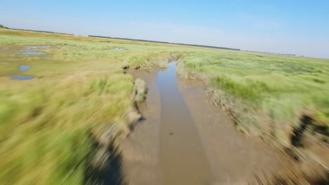 Disparo-De-Drones-Fpv-De-Alta-Velocidad-Rastreando-Un-Estrecho-Río-Fangoso-Que-Refleja-Un-Cielo-Azul-Claro,-En-Un-Parque-Natural-En-Zelanda,-Los-Países-Bajos