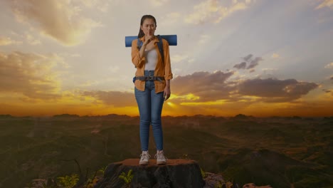 cuerpo lleno de excursionista femenina asiática con mochila de montañismo mirando a la cámara y haciendo un gesto de silencio mientras está de pie en la cima de la montaña durante el atardecer