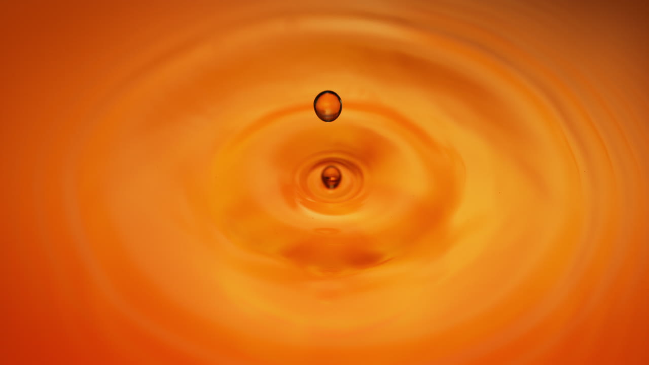 위스키 방울이 매끄러운 금색 액체 시트에 흘러내려서 거시 및 느린 동작으로 파동을 일으킨다.