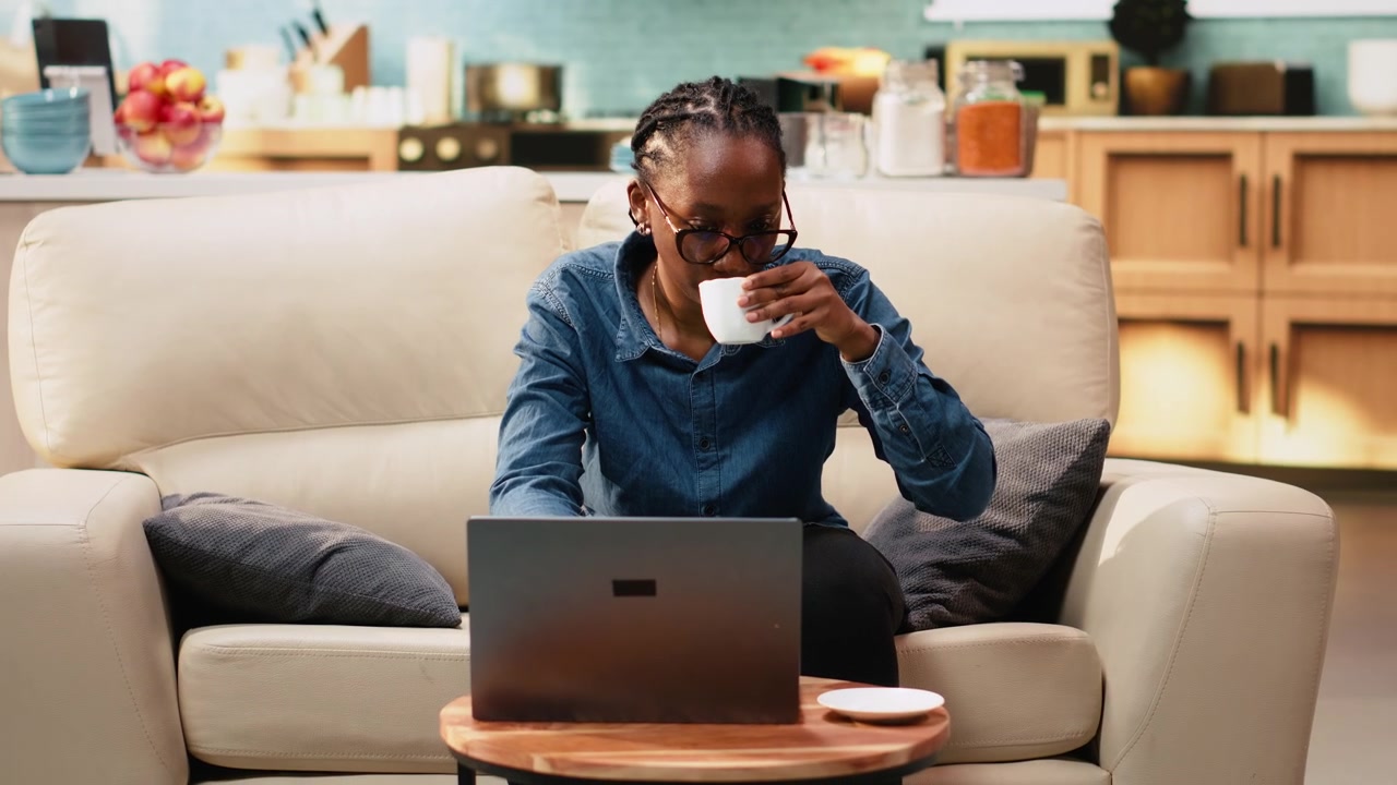 Black woman working remotely from home setup and drinking coffee