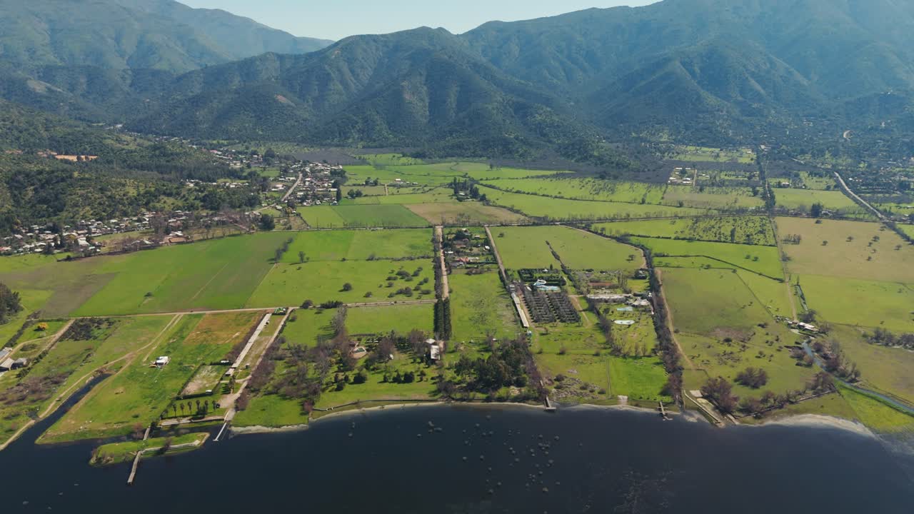 칠레의 아름다운 아쿨레오 호수를 둘러싼 광활한 초록색 을 보여주는 공중 전망, 멀리 있는 산들이 평화로운 시골 풍경을 둘러싸고 있습니다.